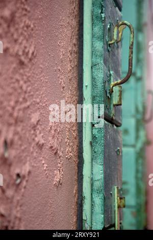 Ein ungewöhnlicher Türgriff an einer grün lackierten Holztür gegen eine rosa lackierte Wand mit abblätternder Farbe Stockfoto
