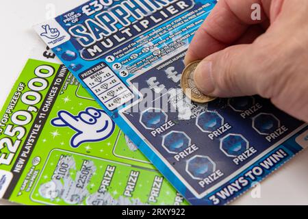 London. UK- 09.27.2023. Zwei Rubbelkarten der National Lottery in weiß isoliert, wobei ein Spieler eine Karte mit einer Münze kratzt. Stockfoto