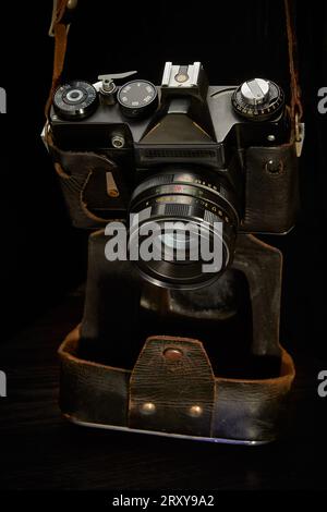 Eine alte Spiegelreflexkamera mit Film-Entfernungsmesser in einer schäbigen Hülle auf dunklem Hintergrund Stockfoto