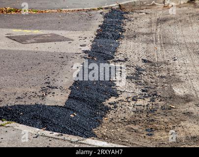 Teilweise renovierte Stadtstraße mit frischen Asphaltflicken, die ungleichmäßige Anwendung und abgenutztes Gehsteig zeigen Stockfoto