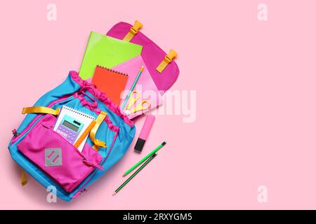 Stylischer Schulrucksack mit verschiedenen Schreibwaren auf rosafarbenem Hintergrund Stockfoto