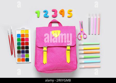 Stylischer Schulrucksack mit verschiedenen Schreibwaren auf grauem Hintergrund Stockfoto