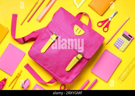 Stylischer Schulrucksack mit verschiedenen Schreibwaren auf gelbem Hintergrund Stockfoto