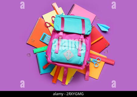 Stylischer Schulrucksack und verschiedene Schreibwaren auf violettem Hintergrund Stockfoto