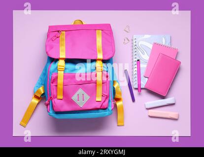 Stylischer Schulrucksack mit verschiedenen Schreibwaren auf farbigem Hintergrund Stockfoto