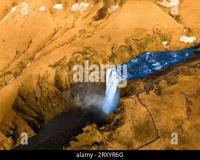Blick aus der Vogelperspektive auf den großen Wasserfall in Island mit dem Bach, der aus gefrorenem Gelände fließt, winterliche Panoramastraße. Unglaubliche isländische Landschaft, die von der majestätischen Skgafoss-Kaskade in der nordischen Region gebildet wird. Stockfoto