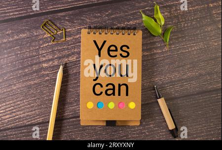 Ja, Sie können Text schreiben. Ein Holztisch und ein Notizbuch mit der Aufschrift „Ja, du kannst“ Stockfoto