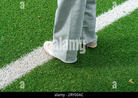 Nahaufnahme der Füße eines Mädchens, die auf dem grünen Kunstrasen-Fußballfeld spazieren Stockfoto