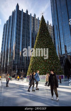 Gleiten Sie anmutig über das Eis, umrahmt vom majestätischen Weihnachtsbaum am PPG Place in der Innenstadt von Pittsburgh, in der Wärme eines sonnigen Wintertages. Stockfoto