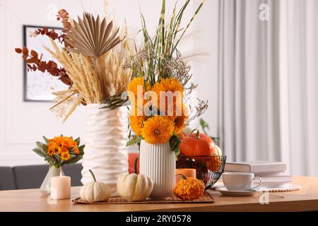 Wunderschöne Herbstkomposition mit leuchtend orangen Blumen, Kürbissen und brennenden Kerzen auf Holztisch im Zimmer Stockfoto