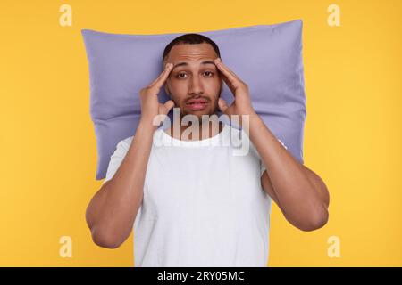 Müder Mann mit Kissen auf orangefarbenem Hintergrund. Schlaflosigkeit-Problem Stockfoto
