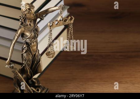 Symbol der gerechten Behandlung nach dem Gesetz. Figur der Lady Justice und Bücher auf Holztisch, Nahaufnahme mit Platz für Text Stockfoto