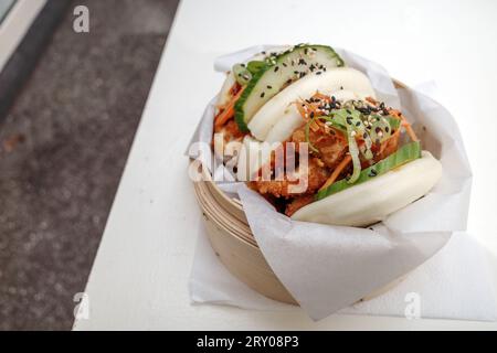 Bao-Brötchen, gedämpftes Weizenmehl auf Basis von gesäuertem Teig, gefüllt mit gebratenem Huhn, auf Bambus-Dampfgarerkorb und weißem Tisch. Stockfoto