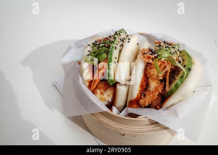 Bao-Brötchen, gedämpftes Weizenmehl auf Basis von gesäuertem Teig, gefüllt mit gebratenem Huhn, auf Bambus-Dampfgarerkorb und weißem Tisch. Stockfoto