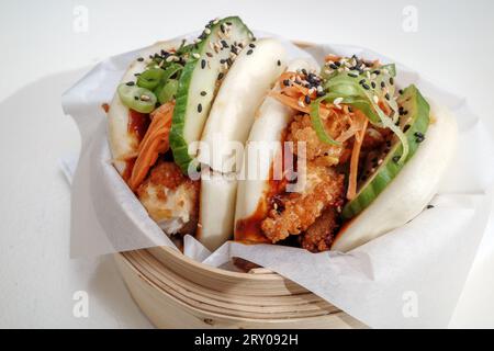 Bao-Brötchen, gedämpftes Weizenmehl auf Basis von gesäuertem Teig, gefüllt mit gebratenem Huhn, auf Bambus-Dampfgarerkorb und weißem Tisch. Stockfoto