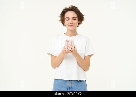 Porträt einer brünetten Frau mit Smartphone, stehend mit Handy, SMS, Bestellung aufgeben, soziale Medien am Telefon durchstöbern, stehen Stockfoto