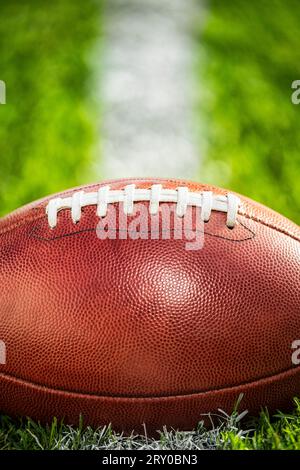 Eine Nahaufnahme eines ledernen American Football, der auf einer weißen Hoflinie im Gras sitzt. Stockfoto