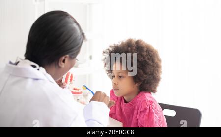 Ein afroamerikanischer Zahnarzt erklärt einem Afro-Kind mit gemischter Rasse, wie man Zähne putzt. Das Arzt- und Gesundheitskonzept für Kinder. Stockfoto