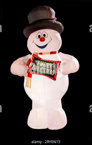Aufblasbarer Schneemann, der ein frohes Weihnachtsschild auf Schwarz isoliert hält. Stockfoto