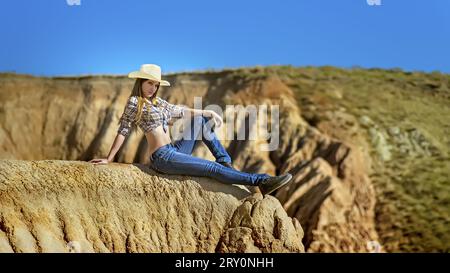 Junge, schöne Frau in Cowboykleidung, sitzt am Rande des Grand Canyon. Stockfoto