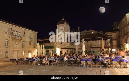 Touristen, die Restaurants auf dem UNESCO-Hauptplatz von Trogir bei Nacht, Kroatien, genießen Stockfoto