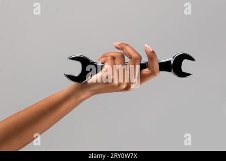 Studioaufnahme einer unbekannten afroamerikanischen Frau mit Schraubenschlüssel in der Hand vor grauem Hintergrund Stockfoto
