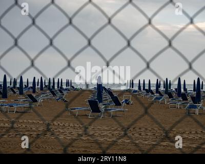 Schlechtes bewölktes Wetter in der nassen Nebensaison. Am Strand gefalteter Sonnenschirm, regnerische Wolken über dem dunklen Meer. Stockfoto