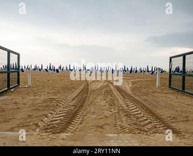 Nasse Liegen und Sonnenschirme am Strand bei Regen. Rollschirm am Strand gegen dunkle Wolken Stockfoto