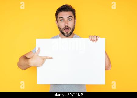 Ein Typ mit leerer Bannerwerbung, isoliert im Studiohintergrund. Ein Mann hält ein leeres Poster mit einem leeren Poster, das mit dem Finger zeigt, und einem Gesten-Index Stockfoto