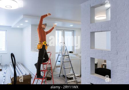 Elektriker repariert Deckenventilator mit Lampen im Innenbereich. Platz für Text. Stockfoto