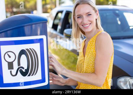 Glückliche Frau überprüft den Reifendruck im Auto Stockfoto