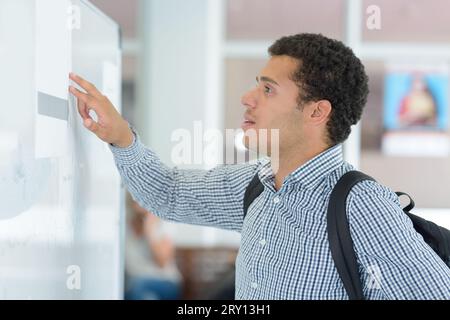 Junge männliche Schülerin, die die Hinweistafel überprüft Stockfoto