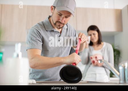 Junge Frau, die auf das männliche Klempnerwaschbecken schaut Stockfoto