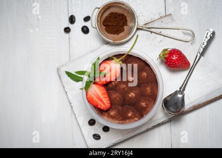 Traditionelles italienisches süßes Dessert aus Tiramisu-Kuchen im Glas auf weißem Holztisch. Mit Erdbeer- und Kakaopulver Stockfoto