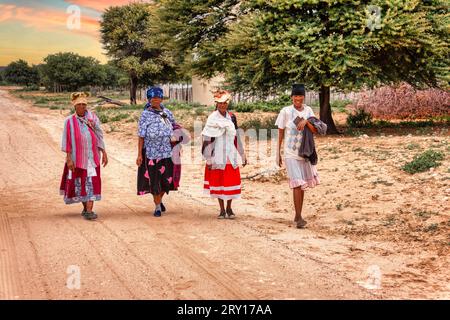 Vier Basarwa-afrikanerinnen, die auf einer unbefestigten Straße im traditionellen Dorf spazieren gehen Stockfoto