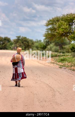 Basarwa afrikanerin, die auf einer unbefestigten Straße im traditionellen Dorf spaziert Stockfoto