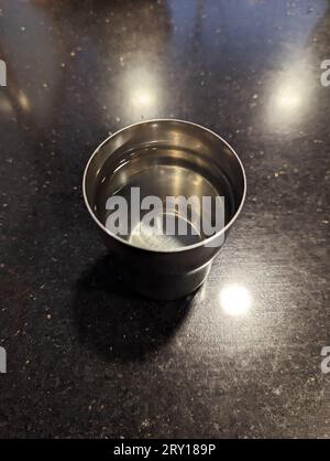 Ein sauberer Edelstahlbecher mit klarem Wasser auf einem glänzenden Tisch Stockfoto