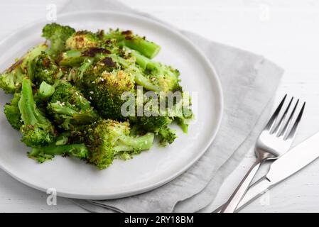 Brokkoli-Blütenstände, gebraten mit Gewürzen und Sesamsamen auf einem Teller auf einem weißen Tisch. Nahaufnahme. Stockfoto