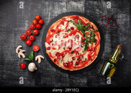 Pizza mit geräucherten Würstchen, Käse, Pilzen, Kirschtomaten, Paprika und Gemüse auf einem Stein und einem schwarzen Kreidebrett, Blick von oben. Stockfoto