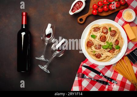 Spaghetti-Pasta mit Fleischbällchen, Kirschtomatensoße, Käse, Weinglas und Flasche auf rostigem Hintergrund, Draufsicht. Stockfoto