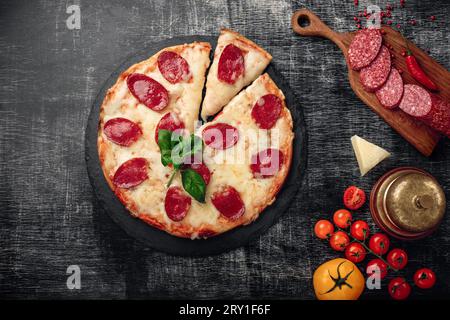 Pizza mit Käse und Salami auf einem Stein und einem schwarzen Kreidebrett, Blick von oben. Stockfoto