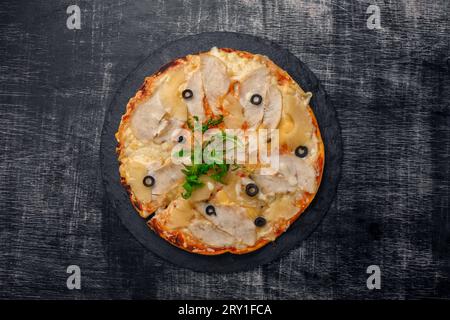 Pizza mit Huhn, Ananas, Käse und Oliven auf Stein und schwarzem Holzgrund. Ansicht von oben. Stockfoto