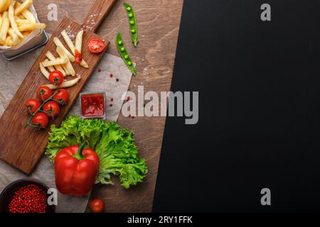 Pommes frites im Gitter mit Ketchup, Salat und Kirschtomaten auf Holztisch. Draufsicht mit Platz für Ihren Text. Stockfoto