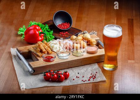 Große Auswahl an Snacks für Bier, darunter frittierte Käsebällchen, Schweineschinken, Schinken und Krabbenstangen, serviert mit Knoblauchsaucen, Ketchup und Senf auf einem Woo Stockfoto