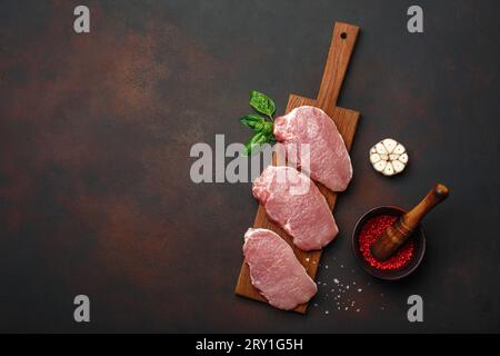 Rohes Schweinesteak mit Basilikum, Knoblauch, Pfeffer, Salz und Gewürzmörtel auf Schneidebrett und rostigem braunem Hintergrund. Draufsicht mit Platz für Ihre T Stockfoto