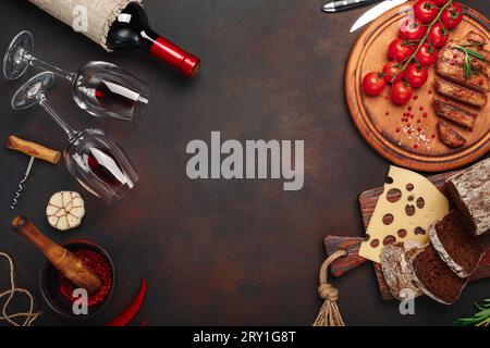 Gegrillte Schweinesteaks in Scheiben auf einem Schneidebrett mit Kirschtomaten, Käse, Brot, Knoblauch und Rosmarin, Flasche Wein, Weinglas, Korkenzieher, Messer, Stockfoto