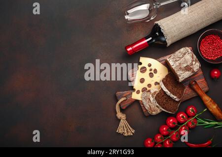 Maasdam-Käse auf einem Schneidebrett mit Kirschtomaten, Schwarzbrot, Knoblauch und Rosmarin, Flasche Wein, Weinglas auf rostigem Hintergrund. Top V Stockfoto