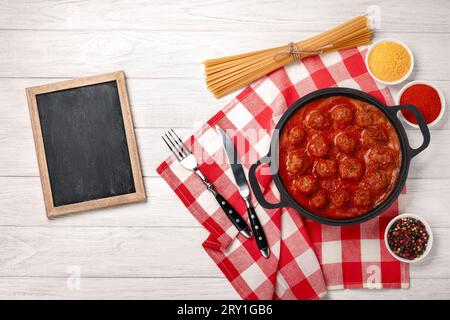 Fleischbällchen in Tomatensauce mit Gewürzen in einer Pfanne auf einem weißen Holzbrett. Draufsicht mit Platz für Ihren Text. Stockfoto