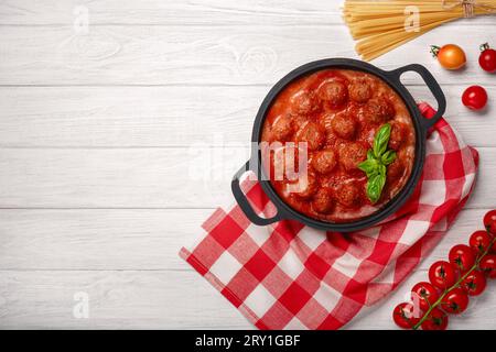 Fleischbällchen in Tomatensoße mit Gewürzen und Basilikum in einer Pfanne und Kirschtomaten auf einem weißen Holzbrett. Draufsicht. Stockfoto
