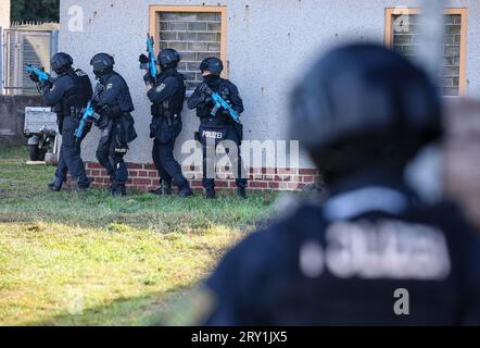 28. September 2023, Sachsen, Wiederau: Offiziere der Einheit Lebel (lebensbedrohliche Einsatzsituationen) rücken in eine Kaserne vor, in der sich zwei Täter verbarrikadiert haben. Rund 150 Auszubildende des Deutschen Roten Kreuzes, der Samariter und der Johanniter aus Sachsen und Sachsen-Anhalt nehmen am Ende einer Trainingswoche an einer inszenierten Terrorsituation Teil. Es gab einen Angriff mit zahlreichen Opfern: Der Täter hat sich verwurzelt, Schüsse werden abgefeuert, es gibt Rauch, schwer bewaffnete und verhüllte Polizisten stürmen das Gebäude. Danach müssen die Notärzte die Verletzten behandeln. Stockfoto